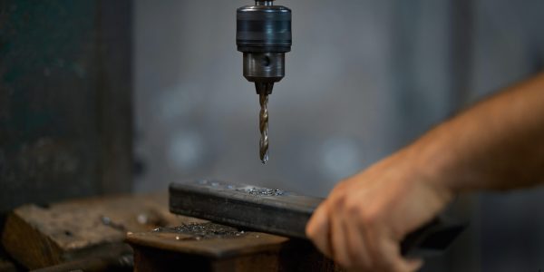 Close up of worker working with drill for creating special details for fence in smithy. Concept of process creating modern and good fence with special equipments.